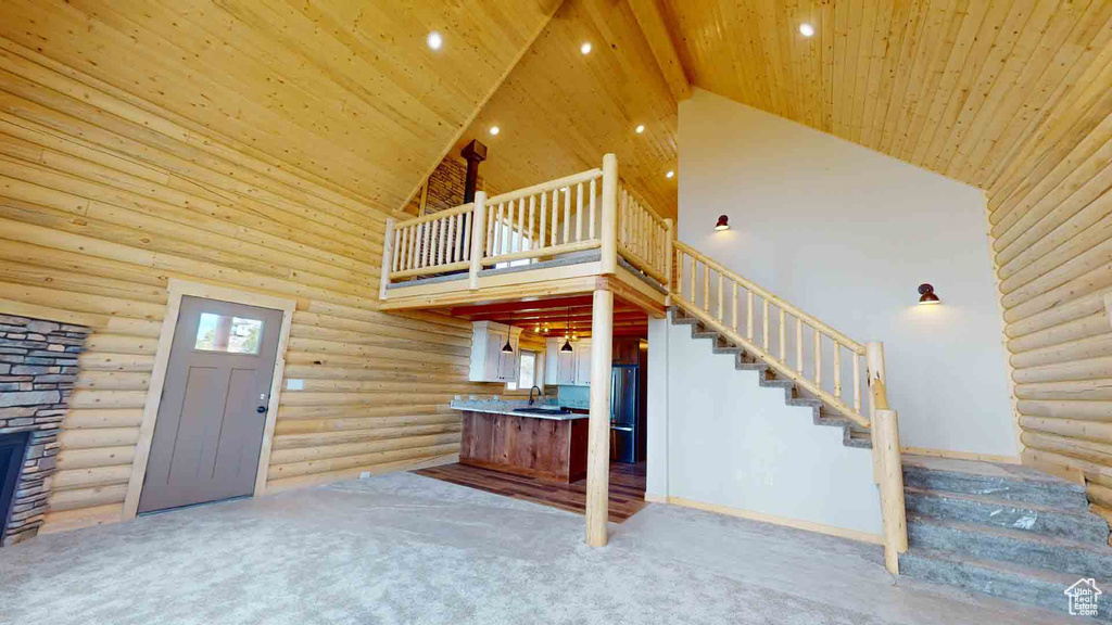 Unfurnished living room featuring high vaulted ceiling, log walls, stairway, carpet, and recessed lighting