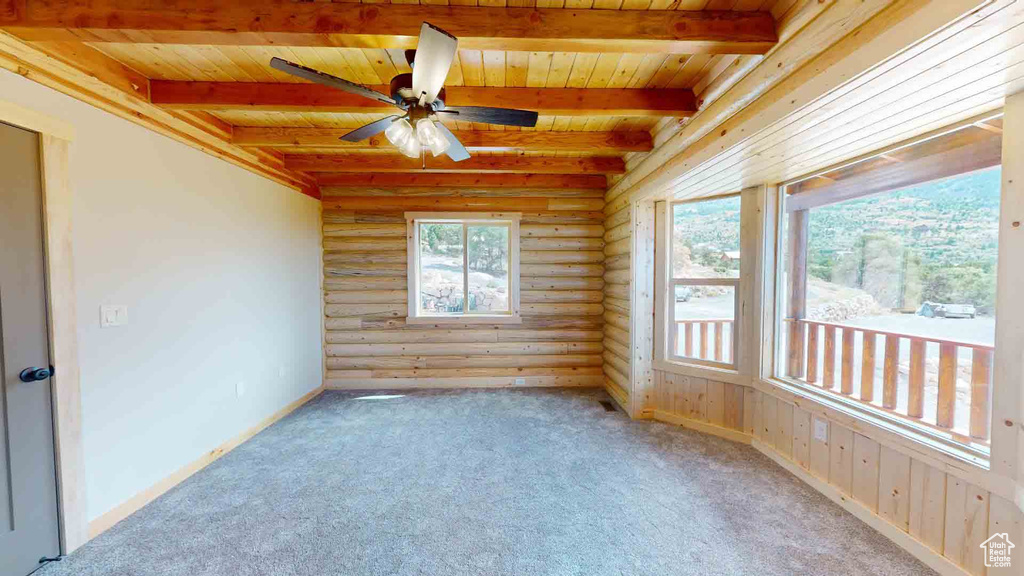 Carpeted empty room with wooden ceiling, rustic walls, beam ceiling, and a ceiling fan