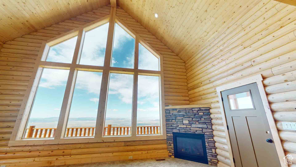 Unfurnished living room with a high ceiling, rustic walls, plenty of natural light, wooden ceiling, and a fireplace