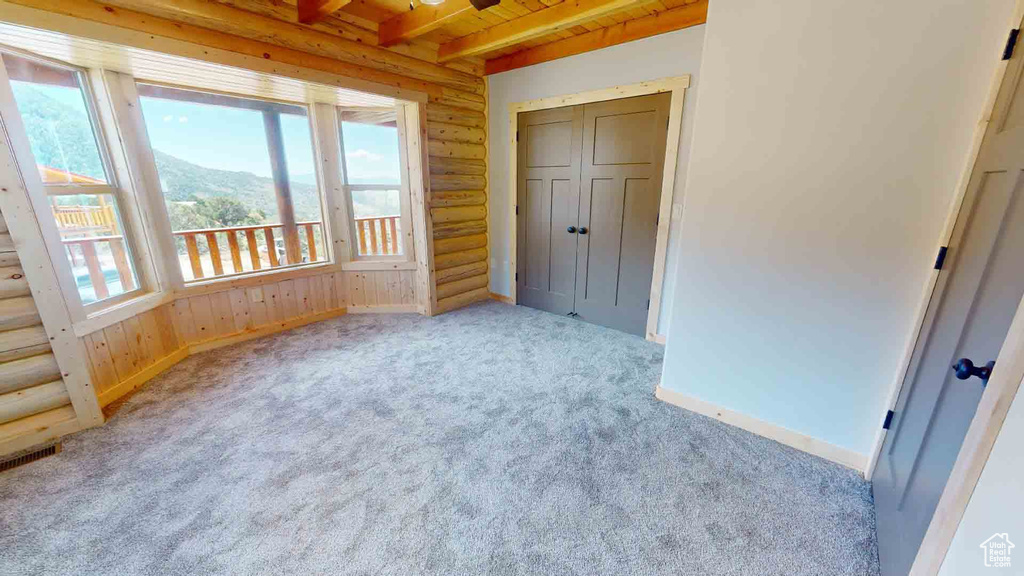Unfurnished bedroom with multiple windows, baseboards, carpet, wood ceiling, and beamed ceiling