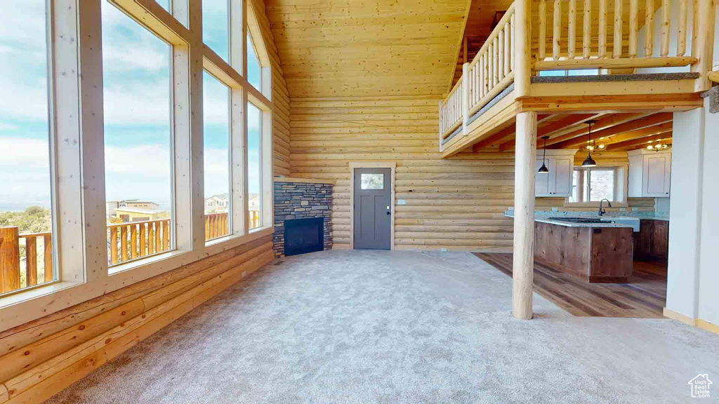 Unfurnished living room featuring log walls, carpet floors, high vaulted ceiling, wood ceiling, and a fireplace