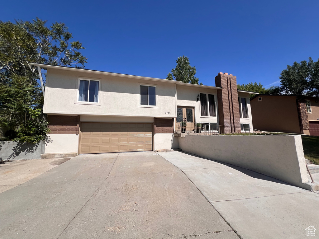View of front of property featuring an attached garage, stucco siding, driveway, a chimney, and french doors