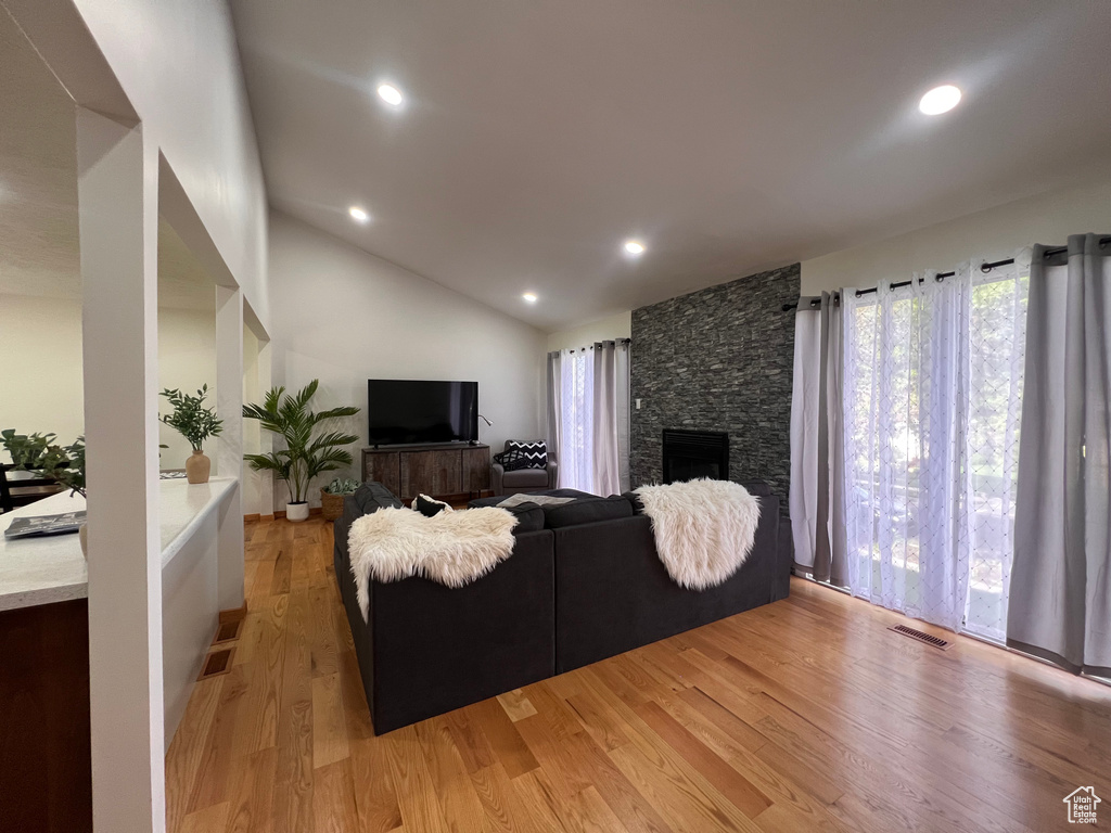 Living room featuring light wood-style floors, lofted ceiling, a stone fireplace, and recessed lighting