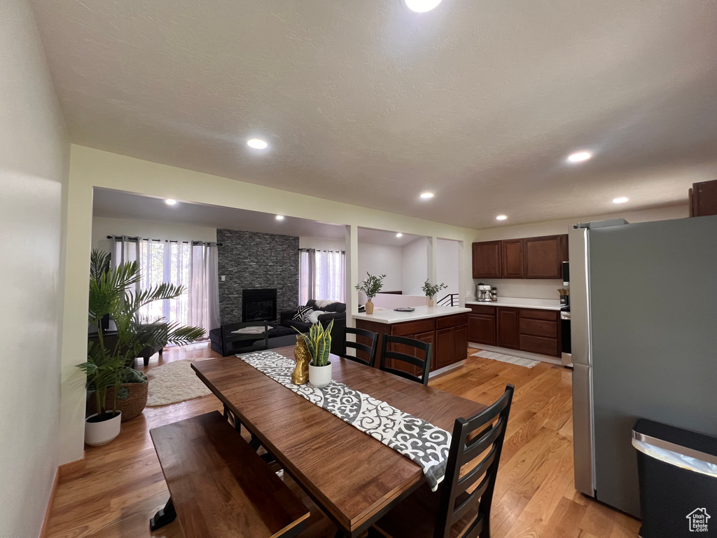 Dining room with light wood-style flooring, a stone fireplace, and recessed lighting