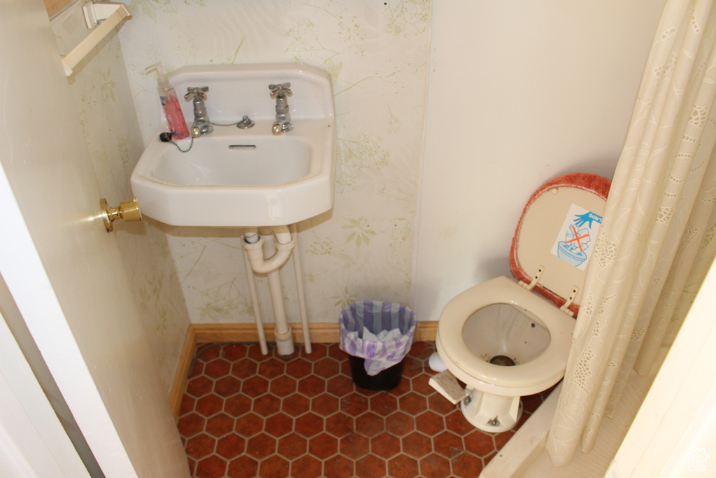 Bathroom with wallpapered walls, a sink, baseboards, toilet, and tile patterned flooring