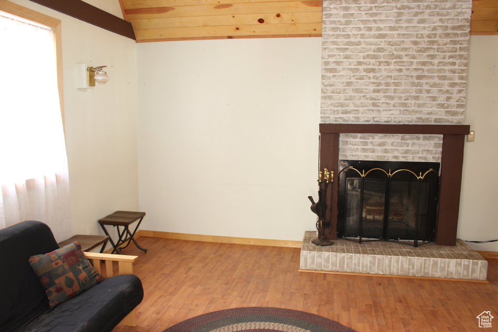 Living area with vaulted ceiling, wood finished floors, baseboards, and a brick fireplace