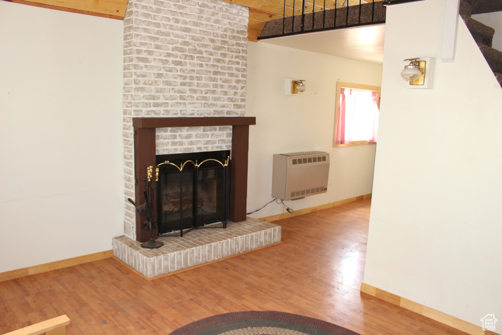 Unfurnished living room with heating unit, baseboards, wood finished floors, and a brick fireplace