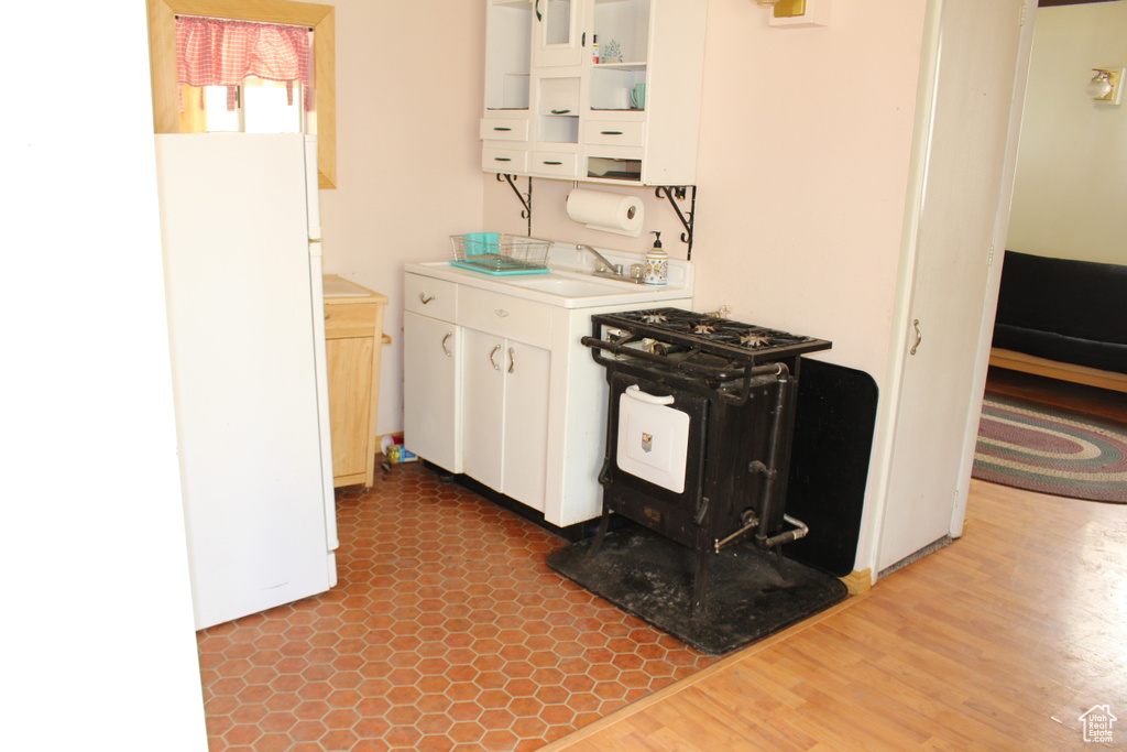 Kitchen featuring freestanding refrigerator, a sink, white cabinetry, wood finished floors, and light countertops