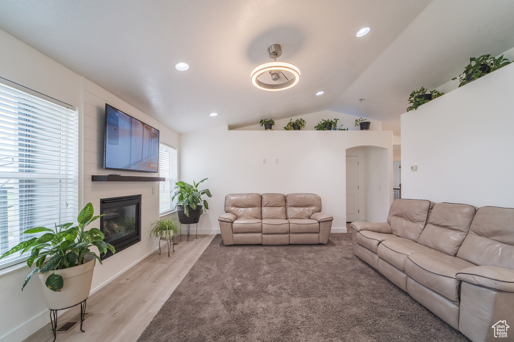 Living area featuring vaulted ceiling, a large fireplace, arched walkways, recessed lighting, and light wood-style floors