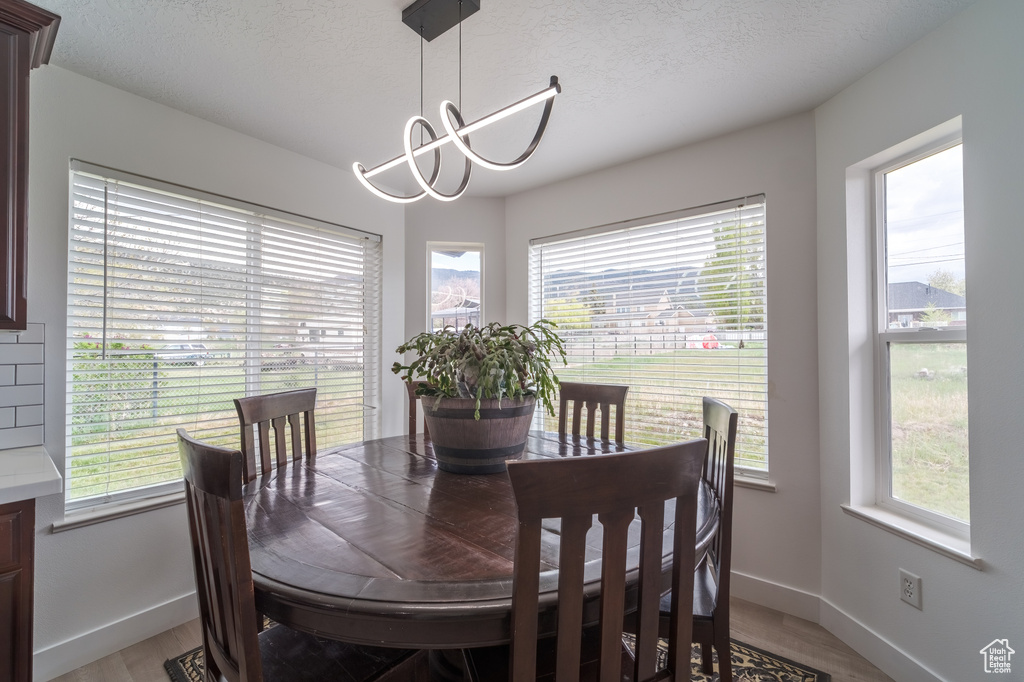 Dining space with light wood finished floors, a chandelier, baseboards, and a textured ceiling