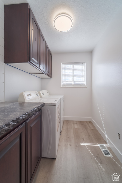 Laundry area featuring washer and dryer, light wood-style flooring, baseboards, cabinet space, and a textured ceiling