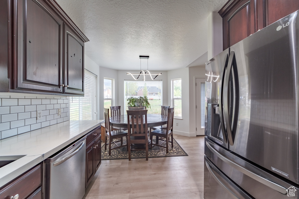 Kitchen featuring appliances with stainless steel finishes, a chandelier, light wood-style floors, tasteful backsplash, and light countertops
