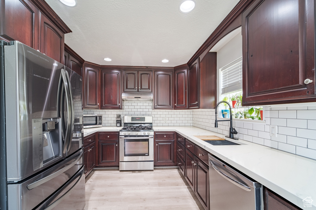 Kitchen with stainless steel appliances, under cabinet range hood, a sink, light countertops, and light wood-style floors