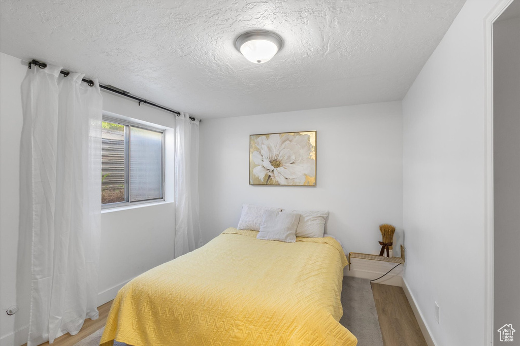 Bedroom with wood finished floors, a textured ceiling, and baseboards