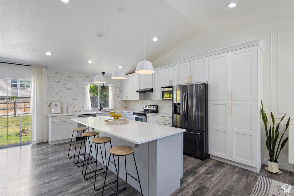 Kitchen with stainless steel appliances, a sink, a kitchen island, dark wood-type flooring, and lofted ceiling