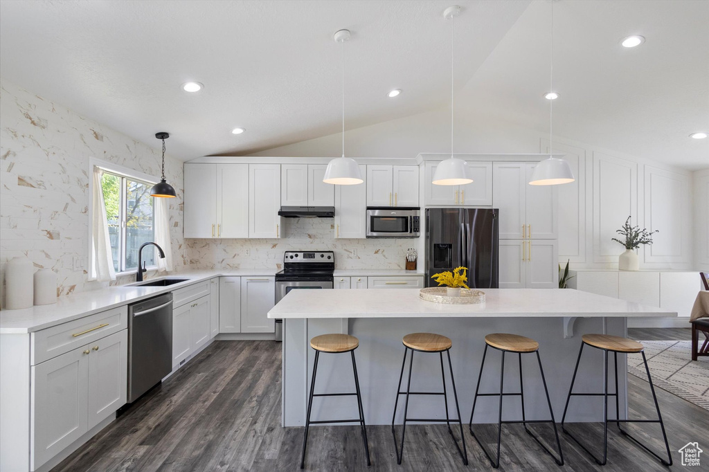 Kitchen featuring stainless steel appliances, a sink, a breakfast bar, vaulted ceiling, and white cabinets