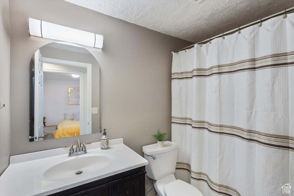 Full bath featuring vanity, toilet, a textured ceiling, and connected bathroom