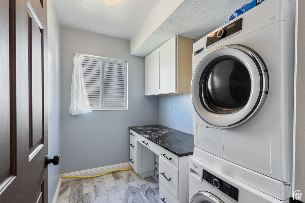 Laundry room with stacked washer and clothes dryer, cabinet space, light marble finish flooring, and baseboards