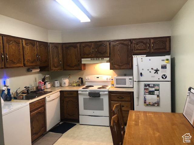 Kitchen with white appliances, under cabinet range hood, washer / dryer, and dark brown cabinets