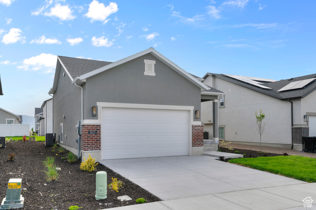 Ranch-style house featuring an attached garage, concrete driveway, stucco siding, brick siding, and cooling unit