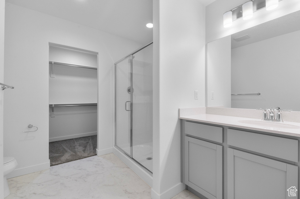 Bathroom featuring marble finish floors, a shower stall, toilet, vanity, and a spacious closet