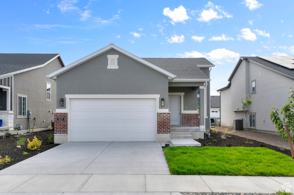View of front of home featuring brick siding, concrete driveway, a garage, central AC, and stucco siding
