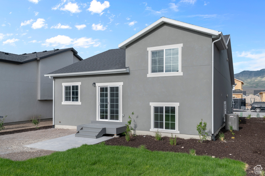 Back of property with cooling unit, a lawn, stucco siding, a mountain view, and a shingled roof