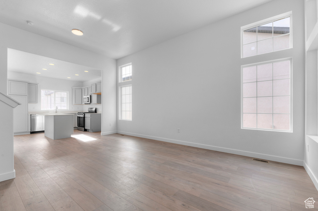 Unfurnished living room with baseboards, light wood-style floors, a sink, and recessed lighting