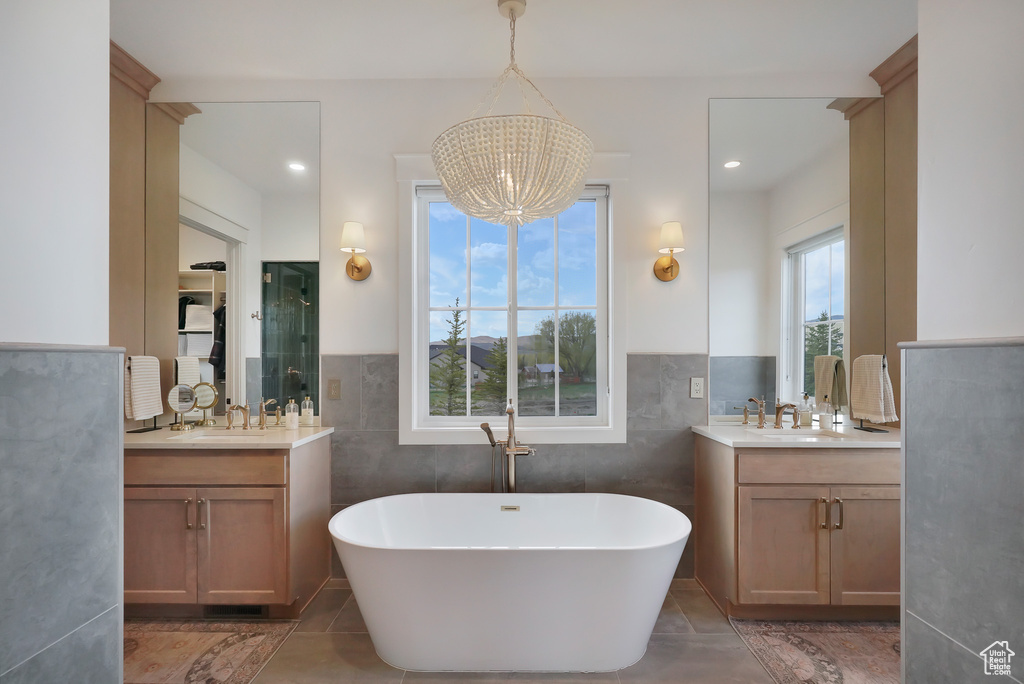 Bathroom with a chandelier, a shower stall, a soaking tub, and two vanities