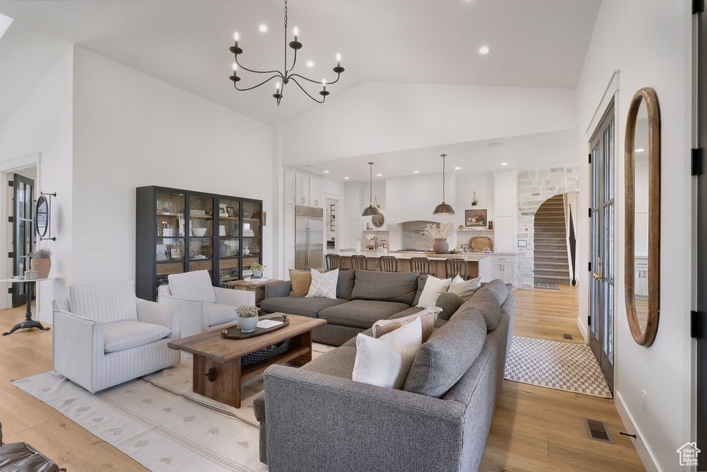 Living room with light wood-type flooring, high vaulted ceiling, a chandelier, arched walkways, and stairs