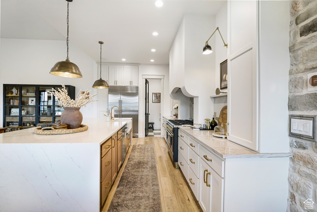 Kitchen featuring high quality appliances, light wood-style flooring, white cabinets, a large island with sink, and pendant lighting