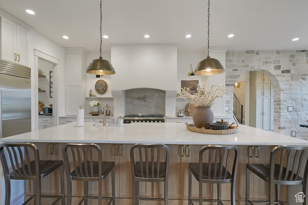 Kitchen featuring arched walkways, stainless steel built in refrigerator, white cabinets, light countertops, and recessed lighting
