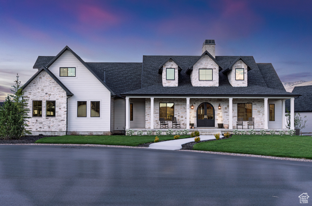 View of front of property with a porch, a chimney, a front lawn, and stone siding
