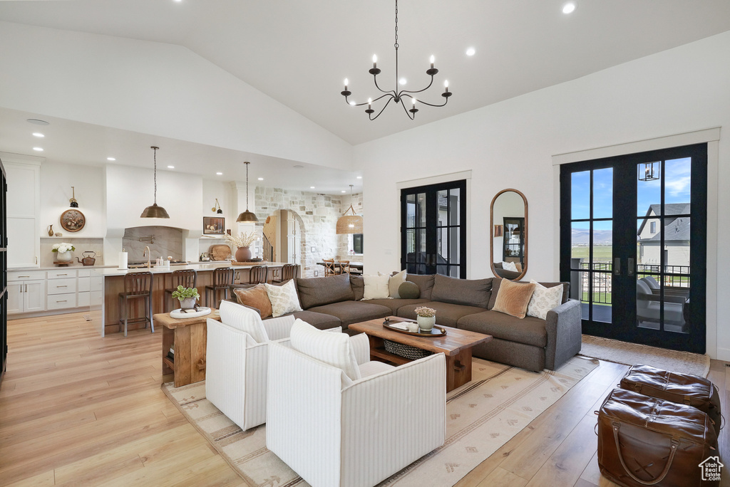 Living room with high vaulted ceiling, light wood finished floors, a chandelier, french doors, and recessed lighting
