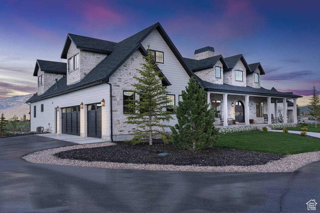 View of side of property featuring asphalt driveway, a porch, stone siding, a chimney, and an attached garage