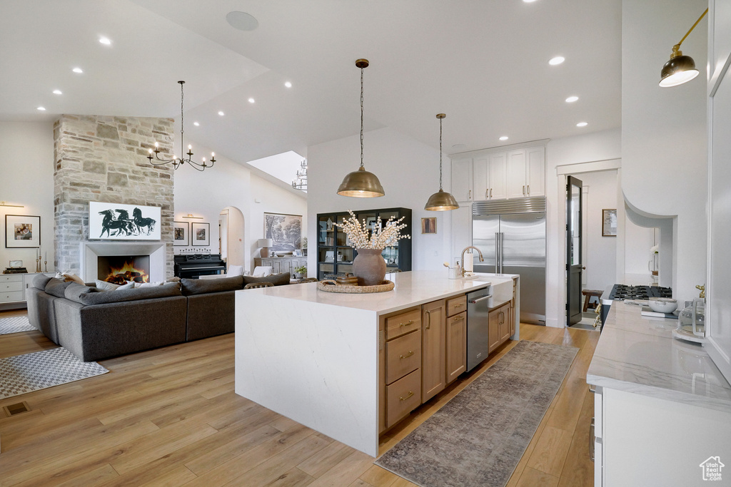 Kitchen with appliances with stainless steel finishes, high vaulted ceiling, light wood finished floors, a fireplace, and decorative light fixtures