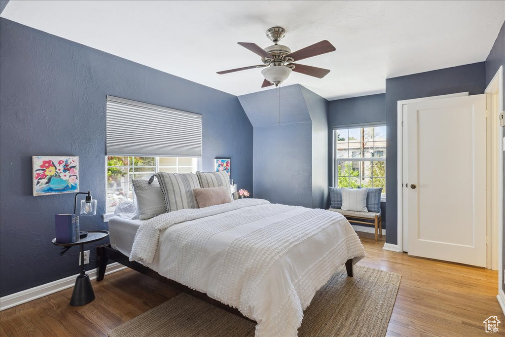 Bedroom featuring a textured wall, multiple windows, light wood-type flooring, baseboards, and a ceiling fan