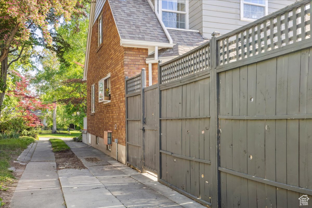 View of property exterior featuring brick siding, a shingled roof, and fence
