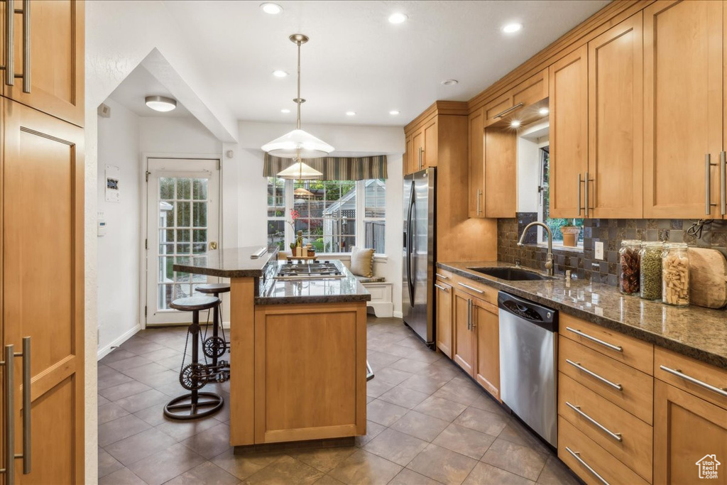 Kitchen featuring stainless steel appliances, a sink, a kitchen island, a breakfast bar area, and tasteful backsplash