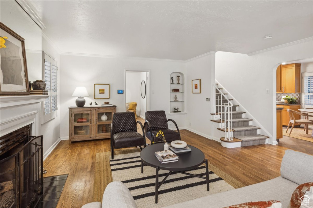 Living area featuring a fireplace with flush hearth, arched walkways, stairs, crown molding, and wood finished floors