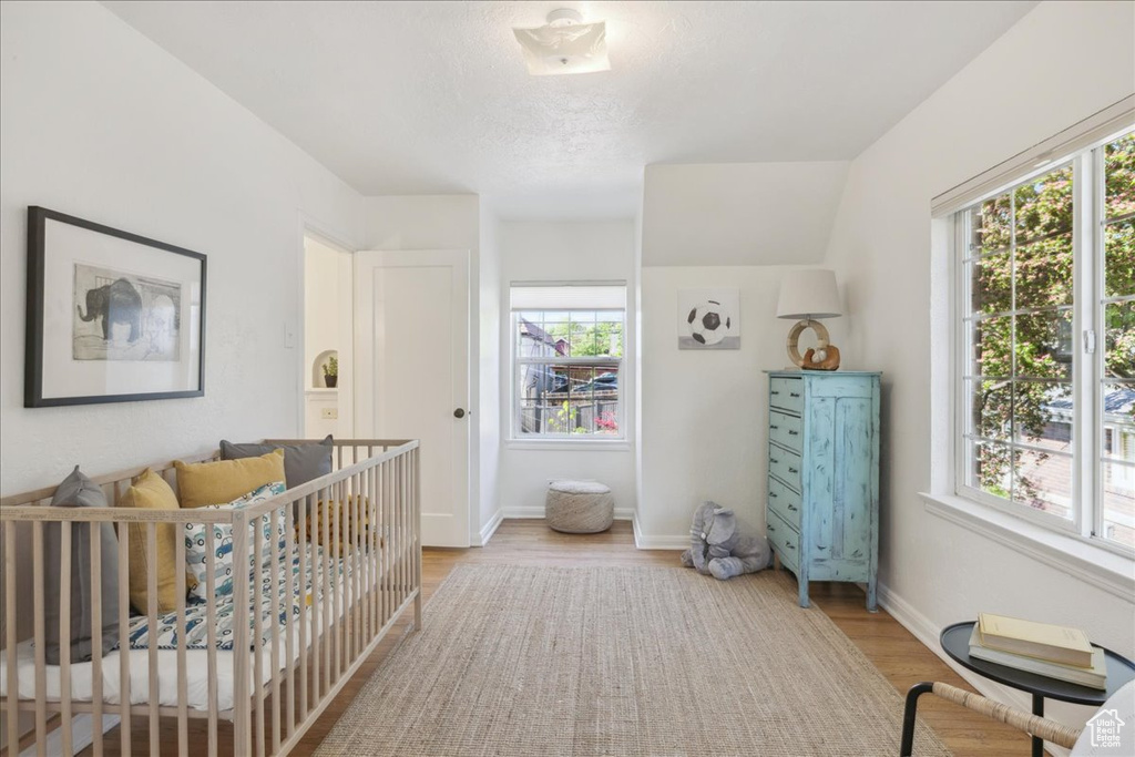 Bedroom featuring multiple windows, light wood-style floors, a nursery area, and a textured ceiling