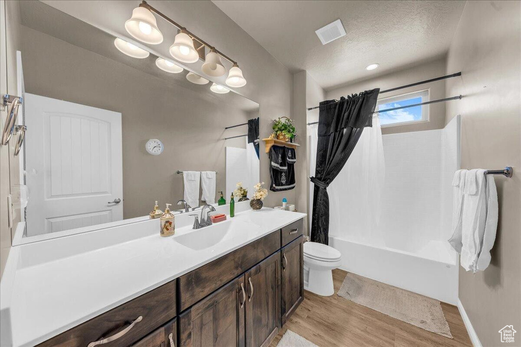 Bathroom featuring wood finished floors, toilet, vanity, shower / bath combination with curtain, and a textured ceiling