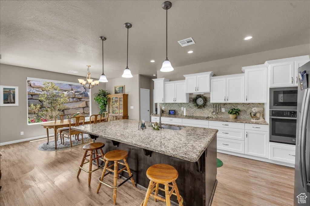 Kitchen with stainless steel appliances, white cabinets, decorative backsplash, a textured ceiling, and a breakfast bar area