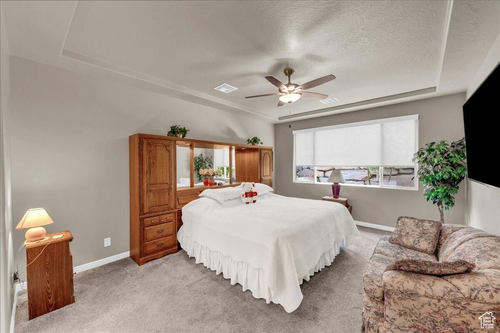 Bedroom with a tray ceiling, light colored carpet, baseboards, a textured ceiling, and a ceiling fan