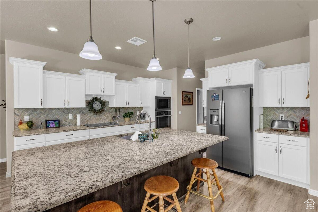 Kitchen with black appliances, a sink, light wood-type flooring, decorative backsplash, and white cabinetry