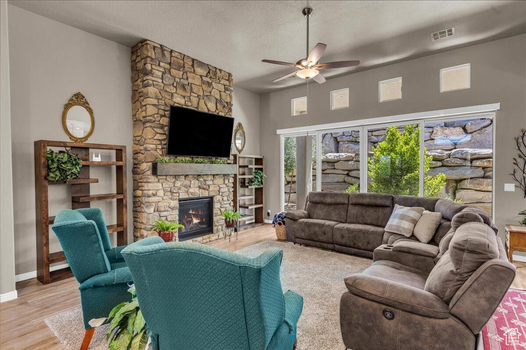 Living area featuring a ceiling fan, a stone fireplace, wood finished floors, baseboards, and a textured ceiling
