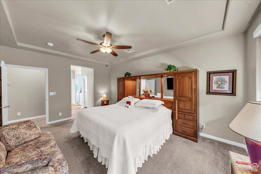 Bedroom featuring a raised ceiling, light carpet, and baseboards