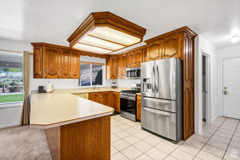 Kitchen featuring stainless steel appliances, a peninsula, a sink, light countertops, and brown cabinets
