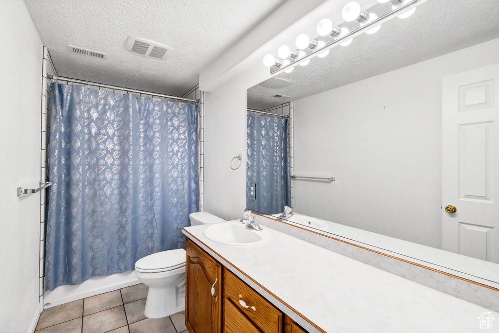 Bathroom featuring a textured ceiling, toilet, vanity, tile patterned floors, and shower / tub combo