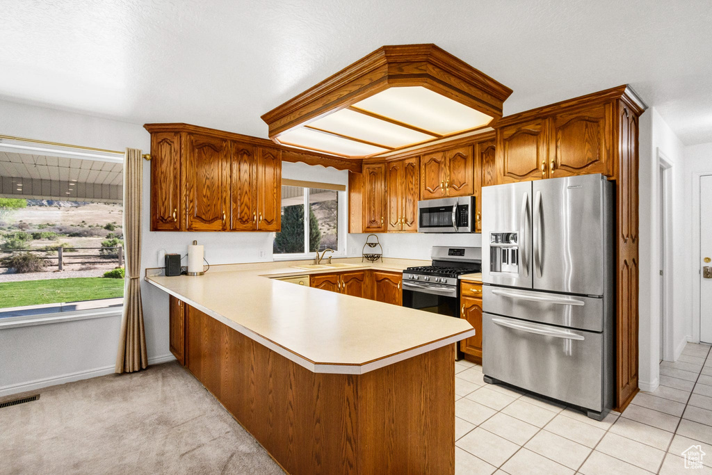 Kitchen with appliances with stainless steel finishes, a sink, light countertops, a peninsula, and brown cabinetry